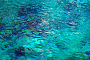 Abstract photo of clear blue water rippling, distorting the dark objects below.