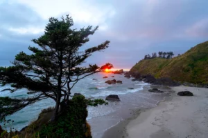 The glowing orange sun finds a break in the clouds just above the horizon at Crescent Beach, Oregon.