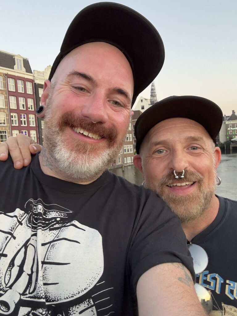 Two men pose for a selfie in the evening in Amsterdam. The man on the left is much taller than the man on the right.