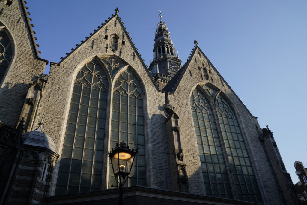 The west facade of de Ould Kerk (the Old Church) in Amsterdam, with it's very tall spire rising above into the blue sky.