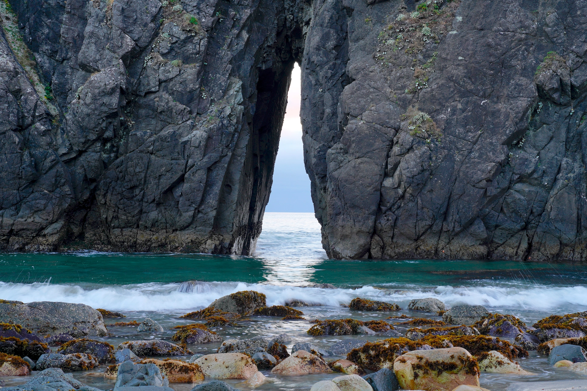 A slit in an ocean rock looks through to a calm evening scene at Harris Beach.