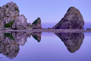 A group of large stone monoliths is reflected in a pool on Harris Beach near Brookings, Oregon.