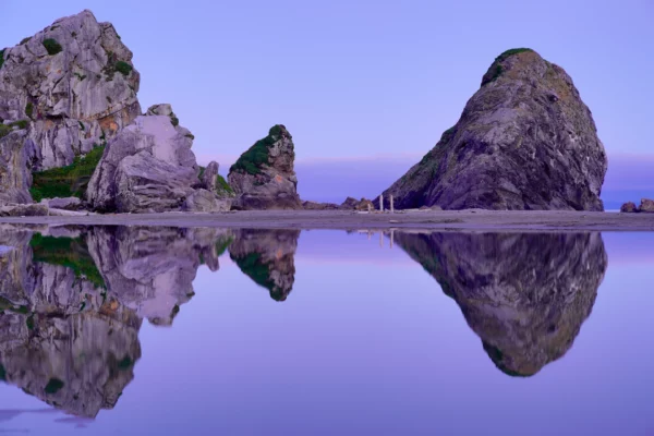 A group of large stone monoliths is reflected in a pool on Harris Beach near Brookings, Oregon.