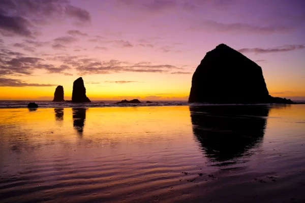 A gold and purple sunset glows behind Haystack Rock and The Needles at Cannon Beach.