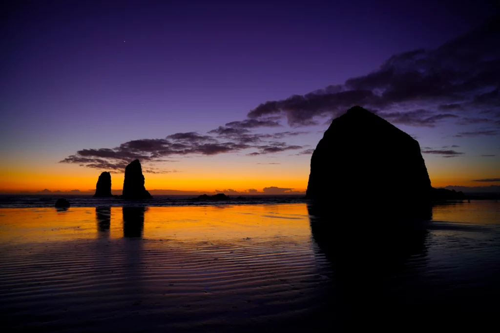 Cannon Beach's Haystack Rock and The Needles stand silhouetted against the last bands of color in a clear Oregon Coast sunset. Venus, "the evening star", shines as a pinpoint of light in the darkening sky.