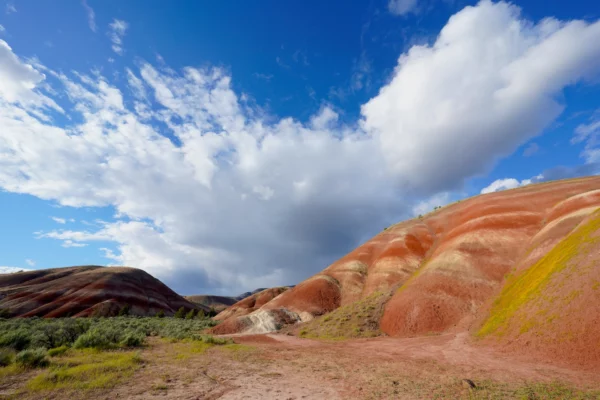 Dramatic clouds appear to burst out from behind hills striped with orange and white claystone.