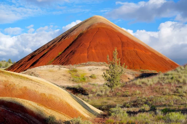 Cone-shaped Red Hill stands boldly in front of a gentle mix of blue sky and clouds surrounded by a brushy desert landscape.