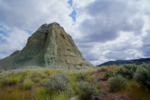 A green hill made of fossilized volcanic ash rises above a sagebrush desert landscape.