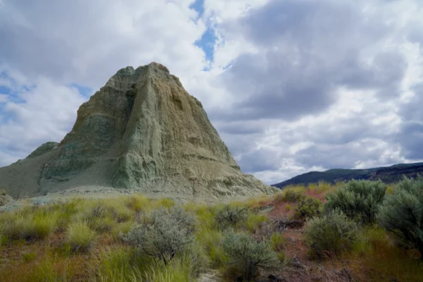 A green hill made of fossilized volcanic ash rises above a sagebrush desert landscape.