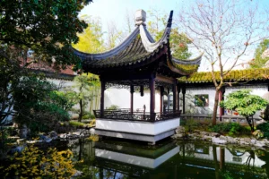 A pavilion with a pointy roof sits waterside within a walled Suzhou-style Chinese garden in Portland, Oregon.