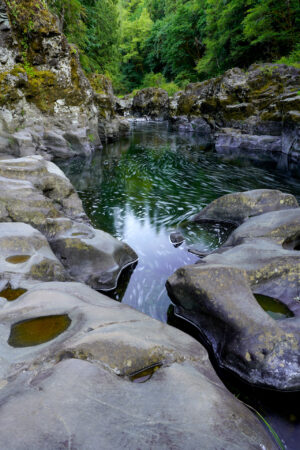 Lines of bubbles trace the current of East Fork Lewis River through a sculpted stone canyon.