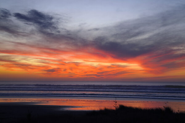 Coral red clouds swirl along the horizon a few minutes after the sun set into the Pacific Ocean at Manzanita Beach.