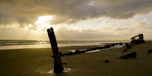 Beams of light shoot through the clouds at Peter Iredale shipwreck on the Oregon Coast.