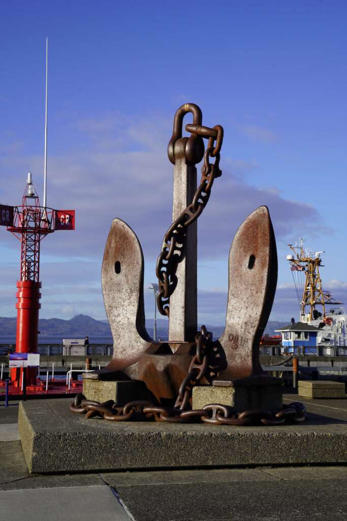 Chains wrap around a massive ship's anchor, standing fifteen feet or more and weighing several tons, displayed outside of Columbia River Maritime Museum.