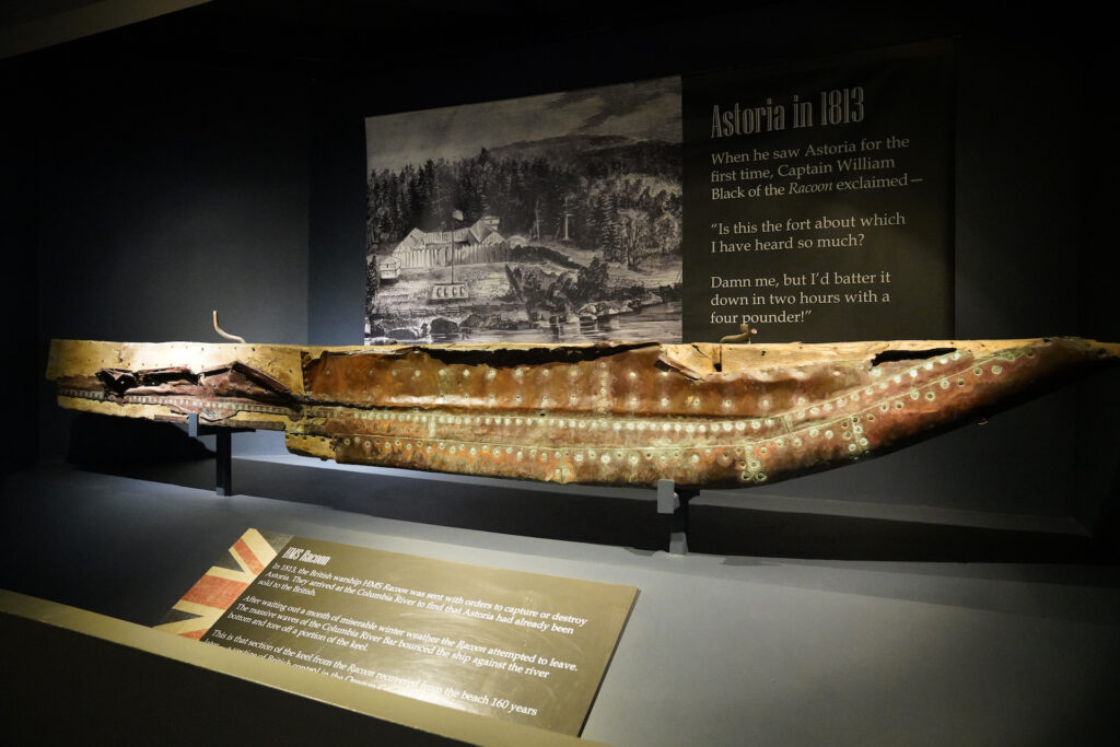 A portion of the keel from HMS Racoon is displayed at Columbia River Maritime Museum with informational signage around it.