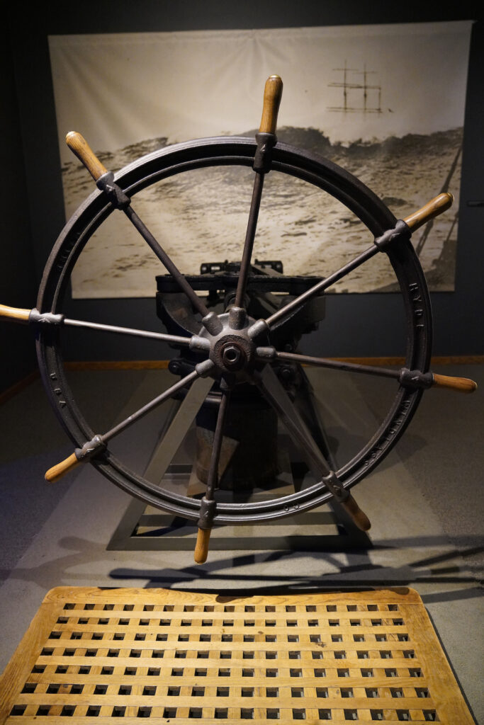 A metal ship's helm with eight spokes ending in wooden handles is displayed at Columbia River Maritime Museum.