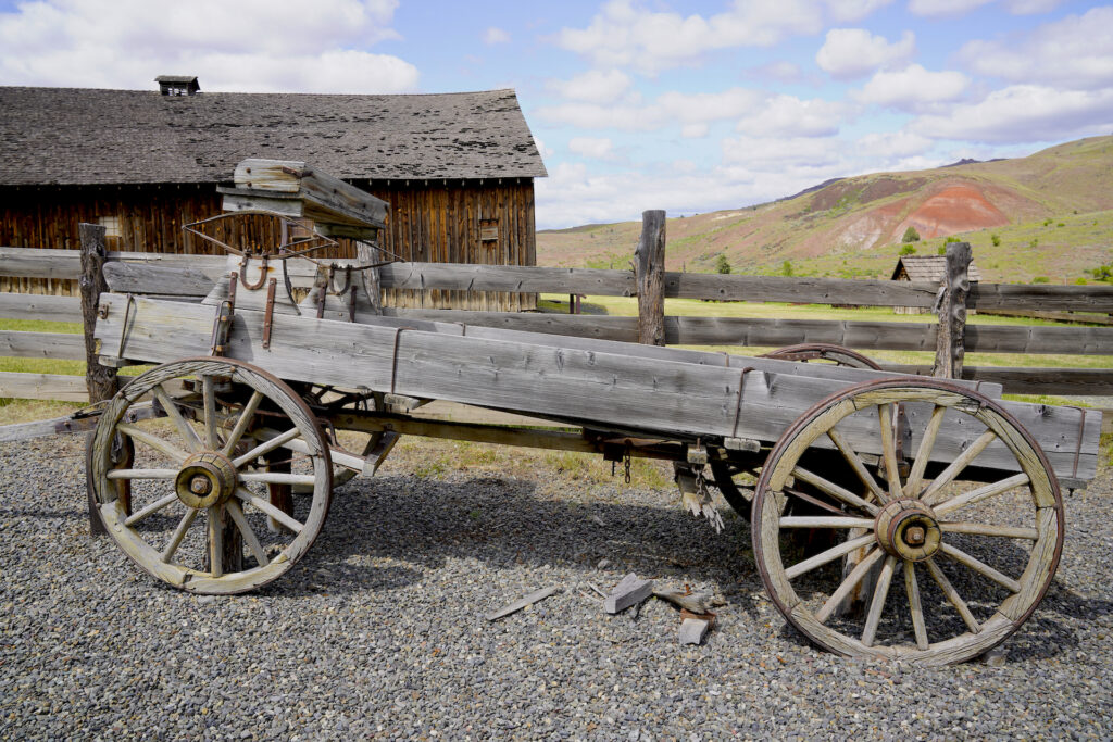 An old wooden cart from the late 1800s sits outside a similarly historic barn at Cant Ranch in the Oregon desert.