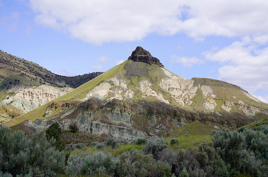 A basalt cap tops Sheep Rock with eroding layers of white, tan, and green claystone below it.