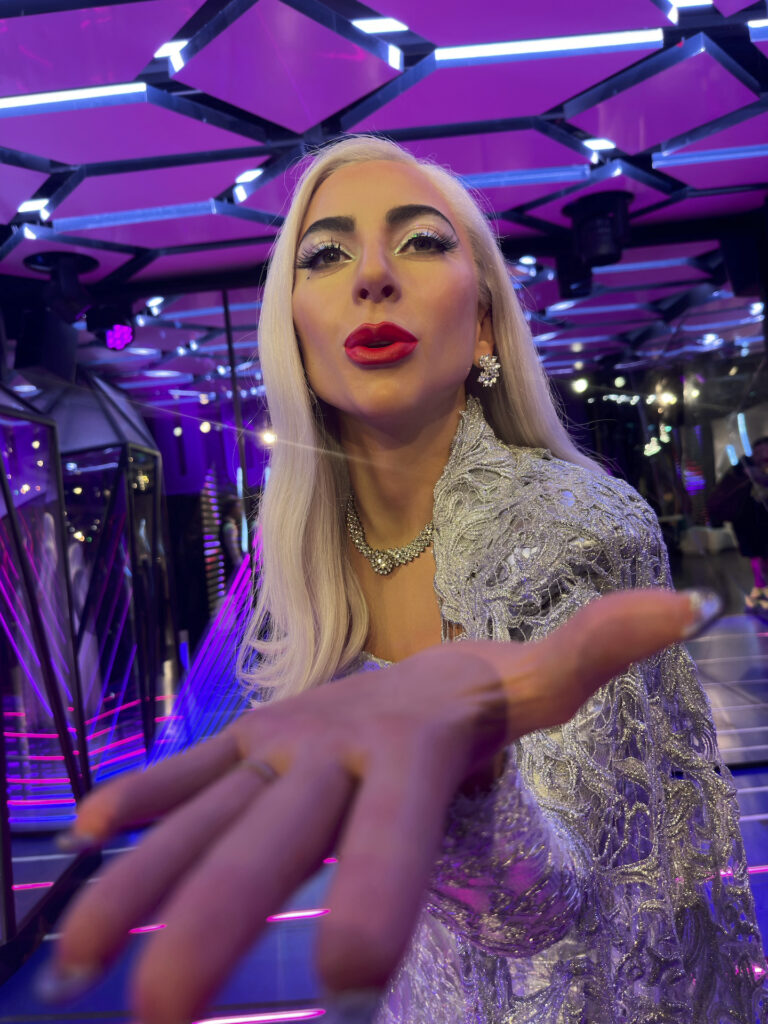 A wax figure of Lady Gaga appears to be blowing a kiss at the camera, her hand outstretched.