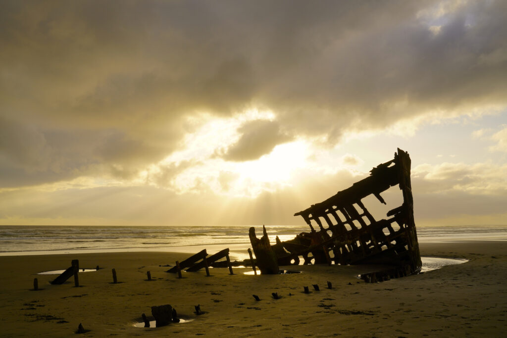 Beams of light shoot through the gathering clouds above the wreck of Peter Iredale on Fort Stevens Beach.