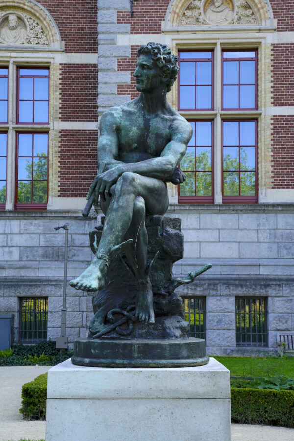 A statue of Mercury, seated, turned green by time, is posed outside Rijksmuseum in Amsterdam.