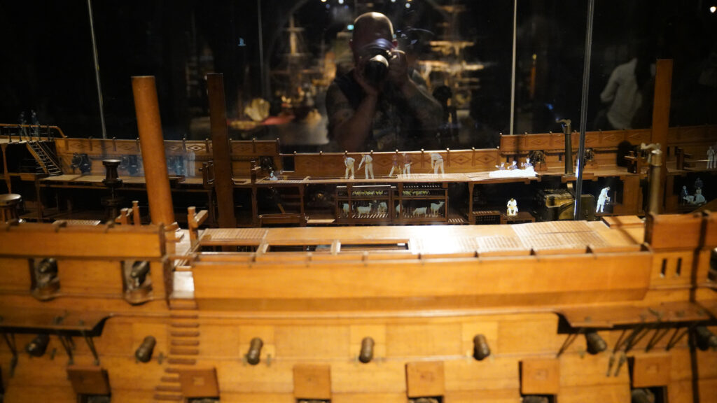 A view of the center portion of a scale model of a large historic sailing vessel. Figures of sailor working on the boat, plus animals in the cargo hold, are holographically projected into the model to provide a sense of scale.