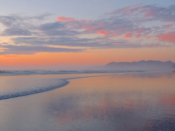 Wet sand reflects the dreamy pinks and blues of a gentle summer sunset at Rockaway Beach.