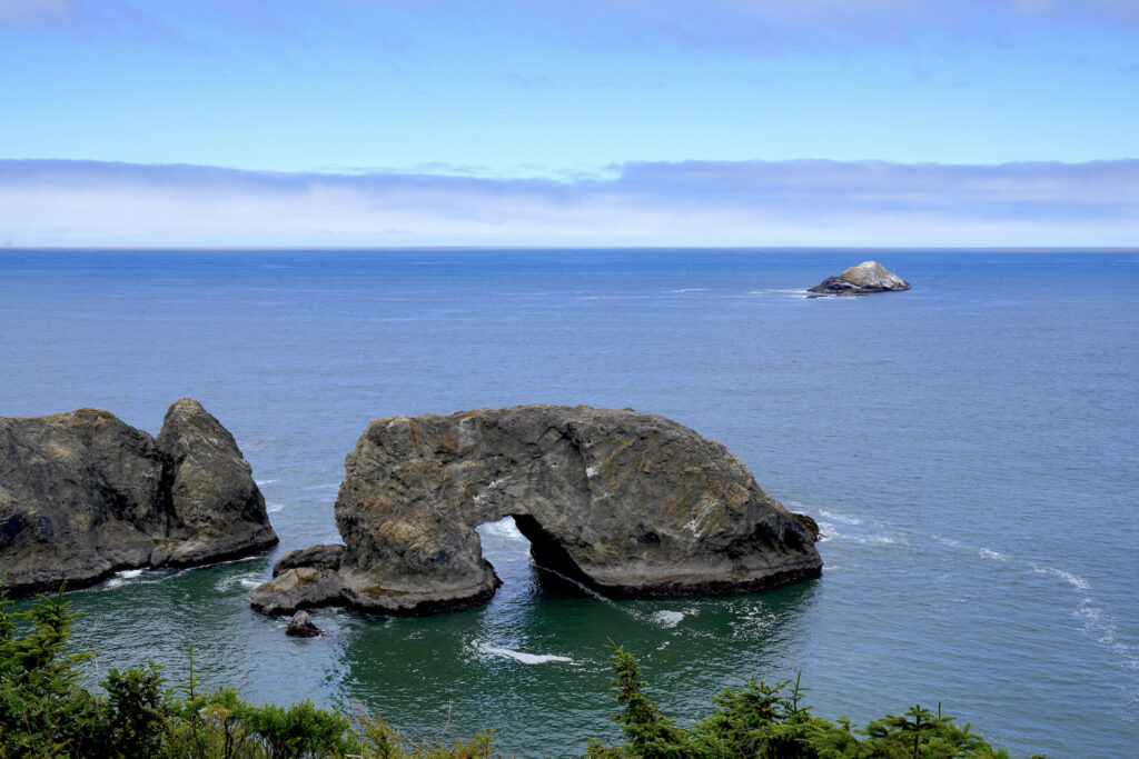 Arch Rock, with it's large crooked hole, rises out of calm seas in Samuel H. Boardman State Scenic Corridor on the Oregon Coast.