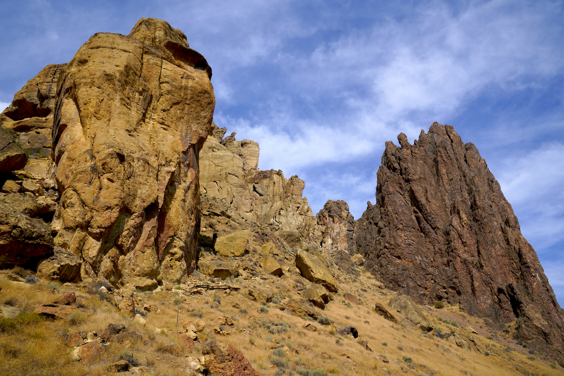 Two tall pinnacles of stone with craggy tops reach up into a blue sky laced with thin clouds at Smith Rock State Park.