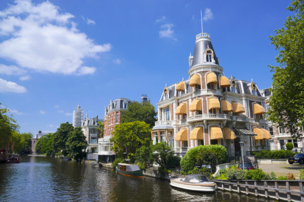 A pretty historic building stands along a canal in Amsterdam on a sunny summer day.