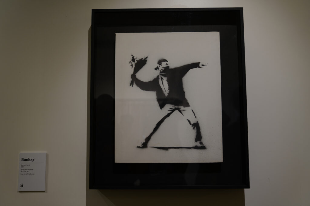 A photo of "The Flower Thrower" by Banksy displayed in a black frame at moco Museum Amsterdam.