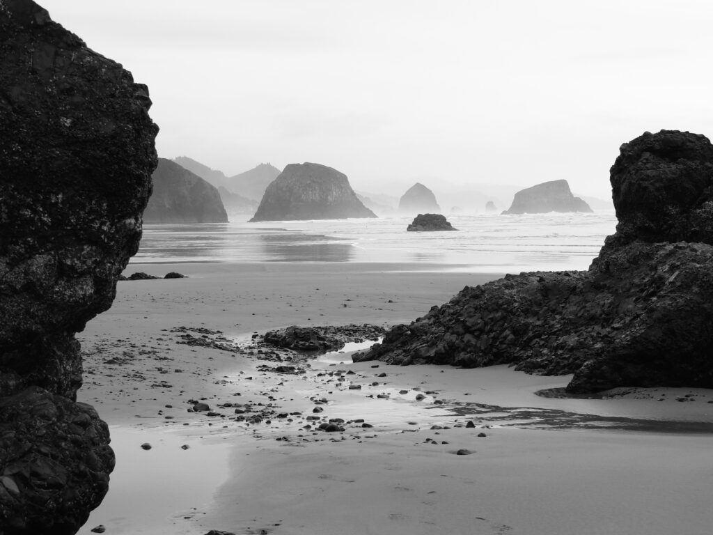 Black and white photograph of a misty, cloudy winter day at Crescent Beach in Ecola State Park, Oregon, with layers of offshore monoliths fading into the gray distance.