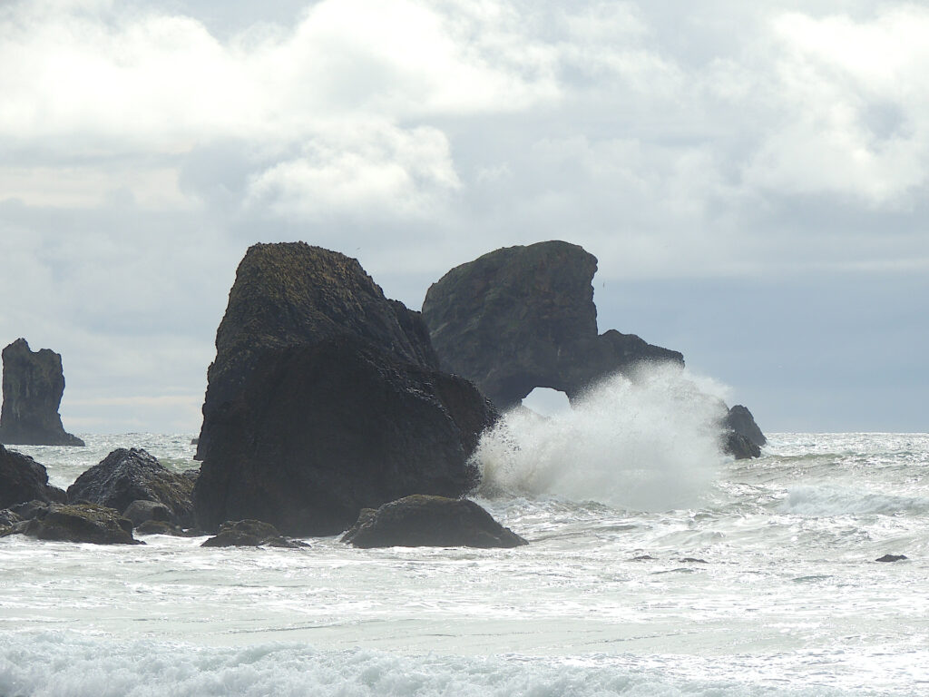 Spray from crashing waves partially obscures an offshore rock arch in Ecola State Park, Oregon.