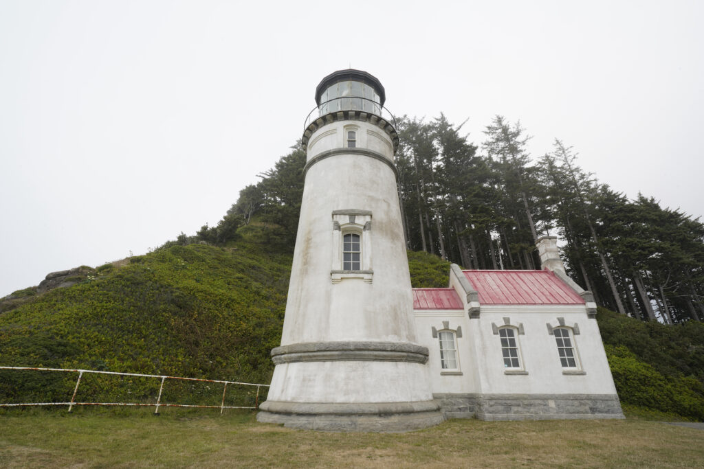 A forested slope rises behind Heceta Head Lighthouse on the Central Oregon Coast.