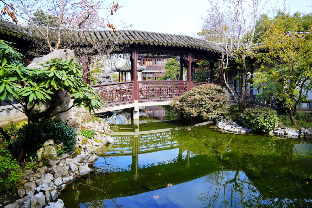 Intricate woodwork and a traditional tile roof decorate a footbridge over the small lake in Lan Su Chinese Garden in Portland, Oregon.