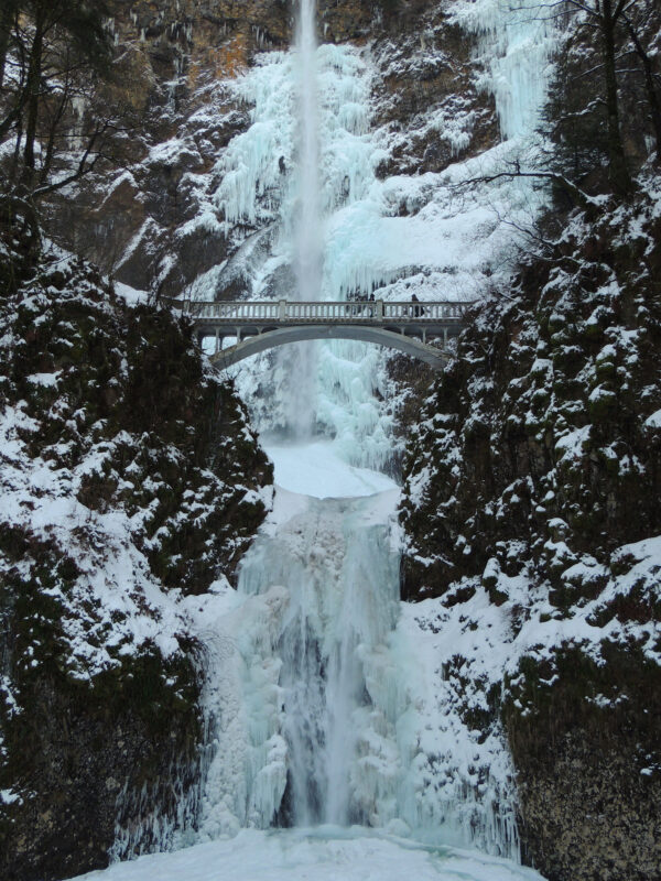 A woman in a cloak crosses the footbridge at icicle-coated Multnomah Falls after a big winter storm.