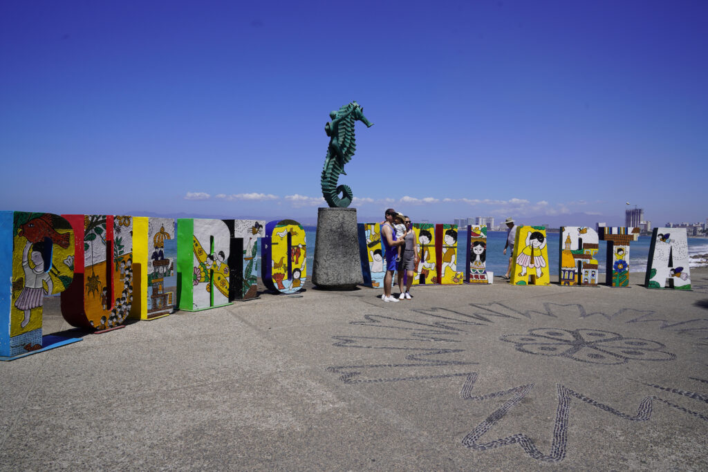 A couple and their toddler pose in front of the famous Puerto Vallarta letters.