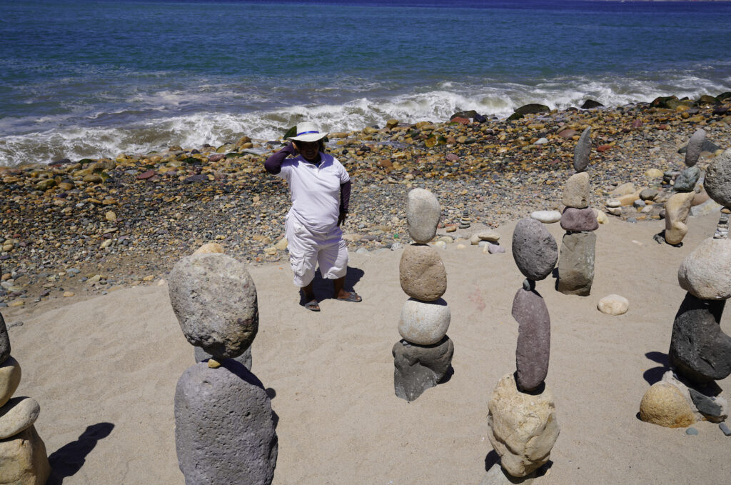 A woman poses behind stacks of stone she created on the beach in Puerto Vallarta.