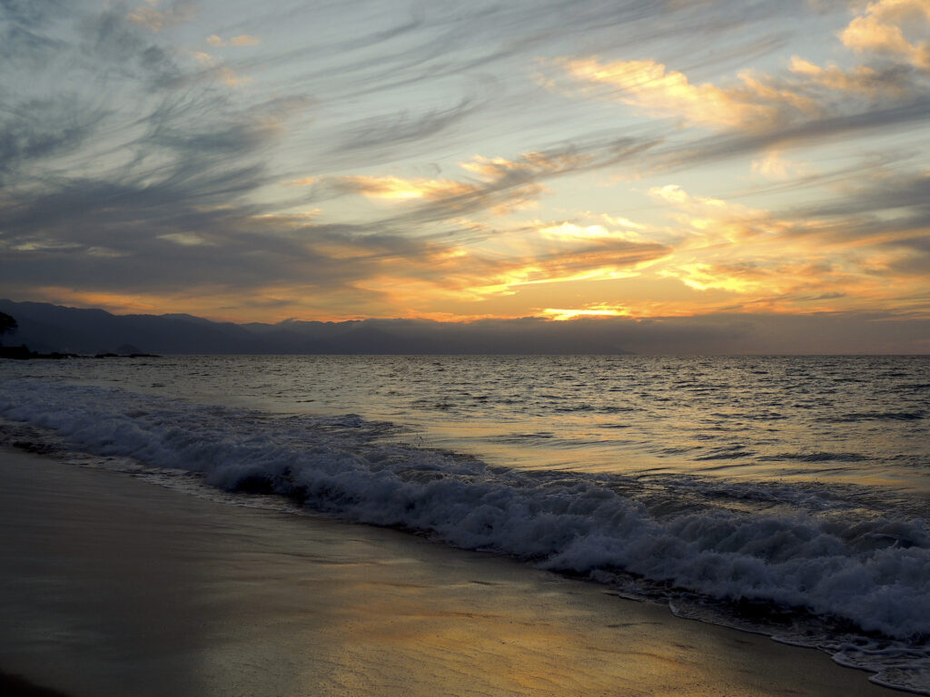 A mix of puffy golden clouds and thin gray clouds like brushstrokes paint a gorgeous sunset at Playa Los Muertos in Puerto Vallarta.