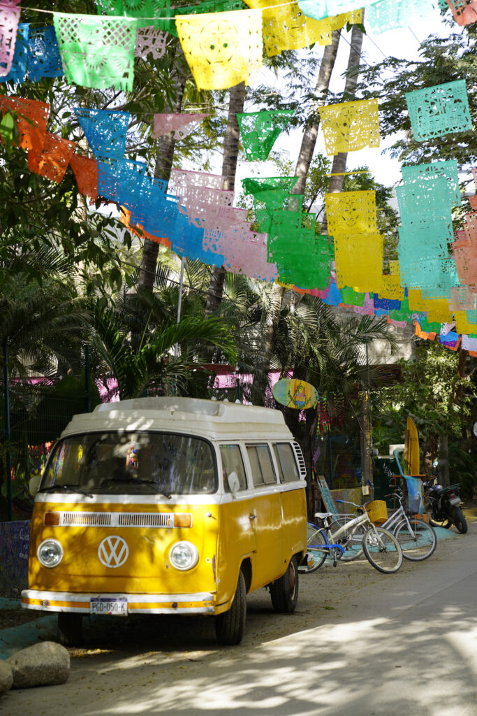 A yellow VW Bus sits beneath colorful  overhead flags in Sayulita Mexico.