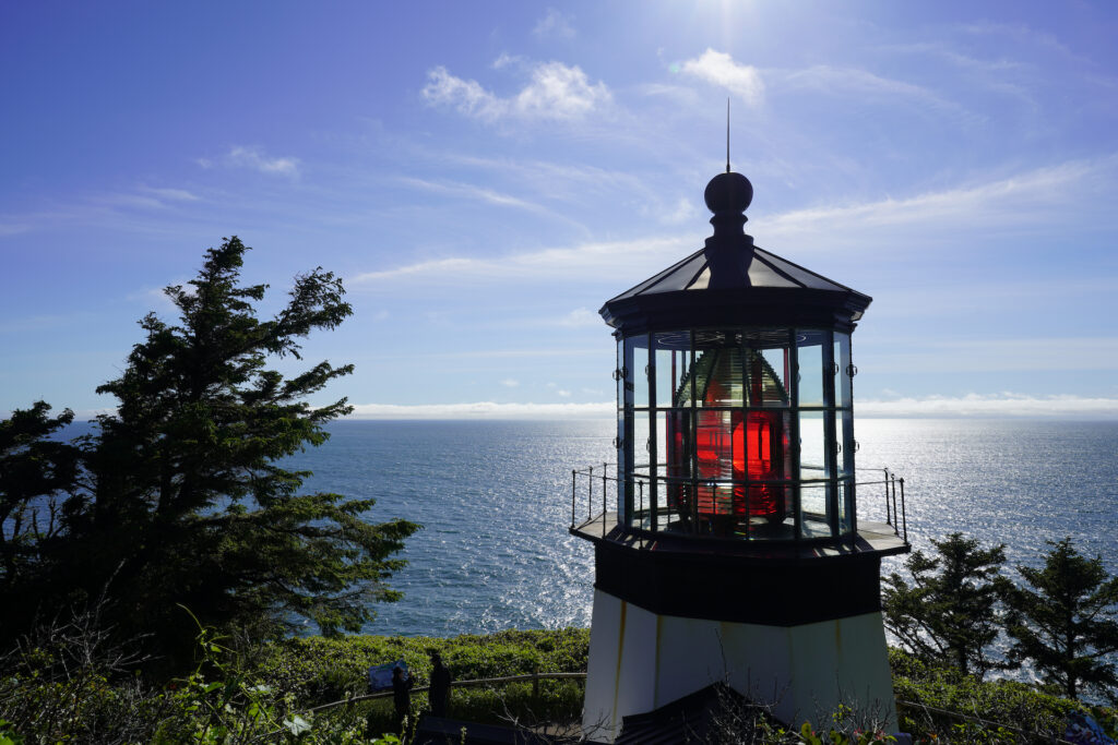 The tower and lens of Cape Meares Lighthouse stand above the Pacific Ocean on a sunny afternoon on the Oregon Coast.