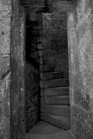 A thin stone spiral staircase is seen winding upwards through a doorway in an old castle.