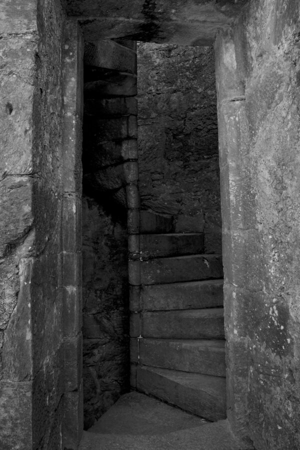 A thin stone spiral staircase is seen winding upwards through a doorway in an old castle.