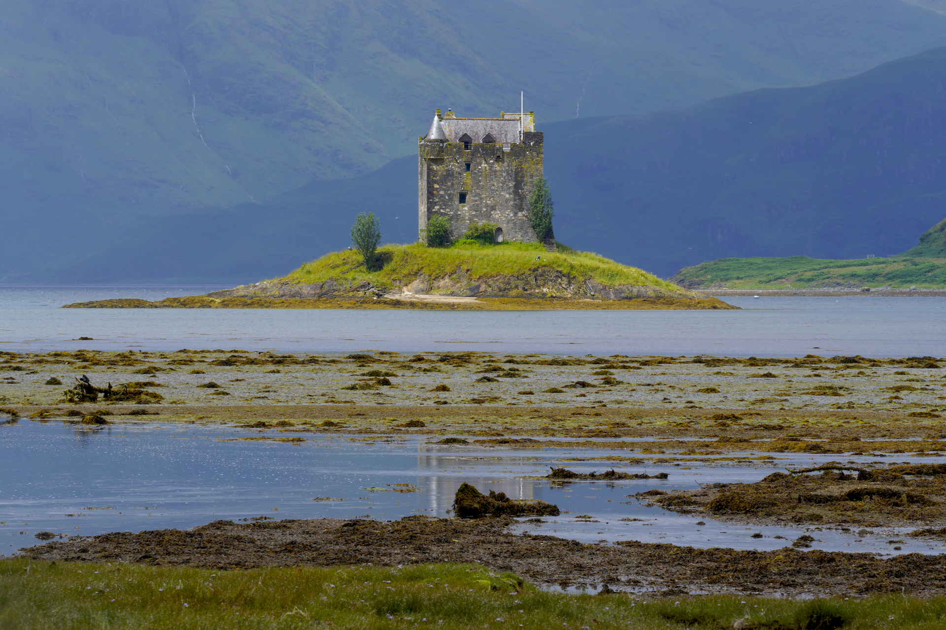 Castle Stalker stands on a small island in Loch Linnhe, reflected in a pool in a tidal flat.