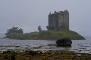 Castle Stalker, a ruin set on an small island, is obscured by moody rain.