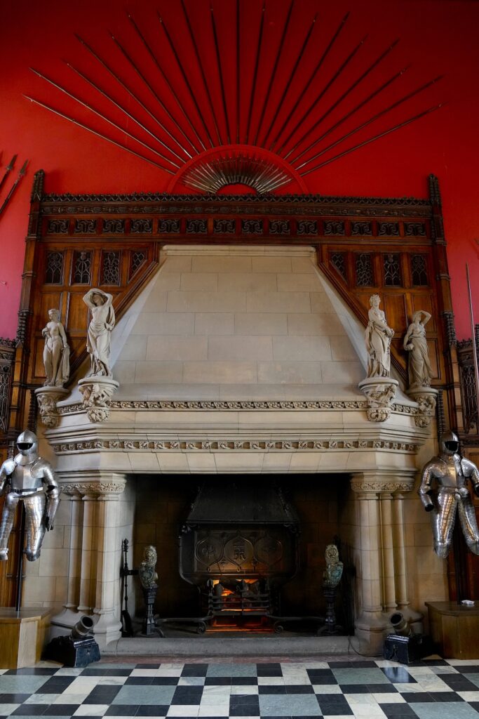 Vivid red walls adorned with suits of armor and spears surround the stone fireplace in the Great Hall of Edinburgh Castle.