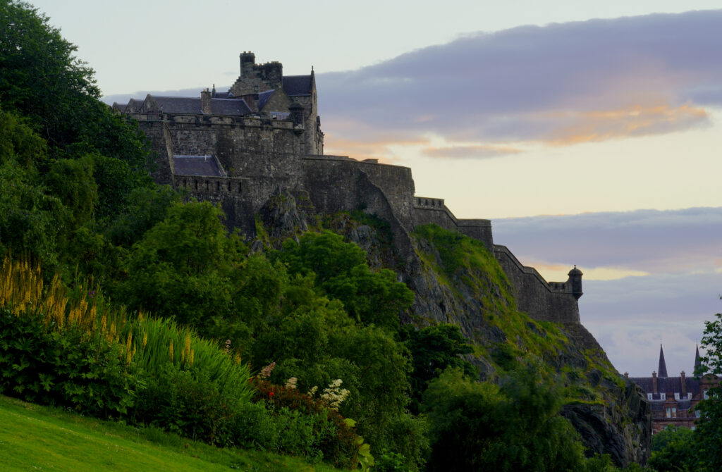 Edinburgh Castle on a windy summer evening with flowers and trees in the foreground.