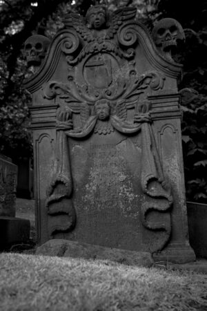 A black and white image of an 1806 headstone at St Cuthbert's in Edinburgh is adorned with angels and skulls.