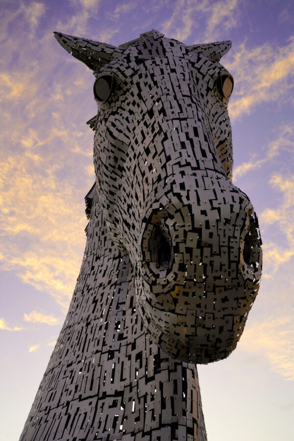 A massive metal sculpture of a horse's face peers down at you with sunset clouds behind it.