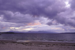 Storm clouds turn purple as dusk approaches at Ganavan Sands beach near Oban, Scotland.